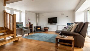 Un salon avec un escalier en bois, une cheminée, un canapé et un téléviseur.