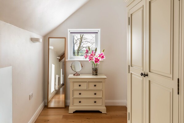 A room with a wooden floor, a white dresser with drawers, a mirror, and a window with a view of trees.