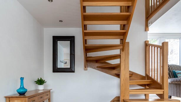 Un escalier en bois, doté d’une rampe et d’un palier avec une petite table et une plante.