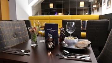 A restaurant setting with a table set for two, including a menu, glasses, a candle, and a bowl of soup with bread.
