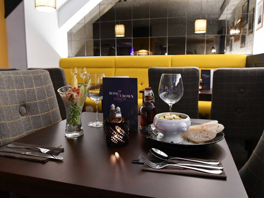 A restaurant setting with a table set for two, including a menu, glasses, a candle, and a bowl of soup with bread.