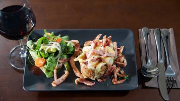 A rectangular plate with a salad and a main dish, accompanied by a glass of red wine and cutlery on a napkin.