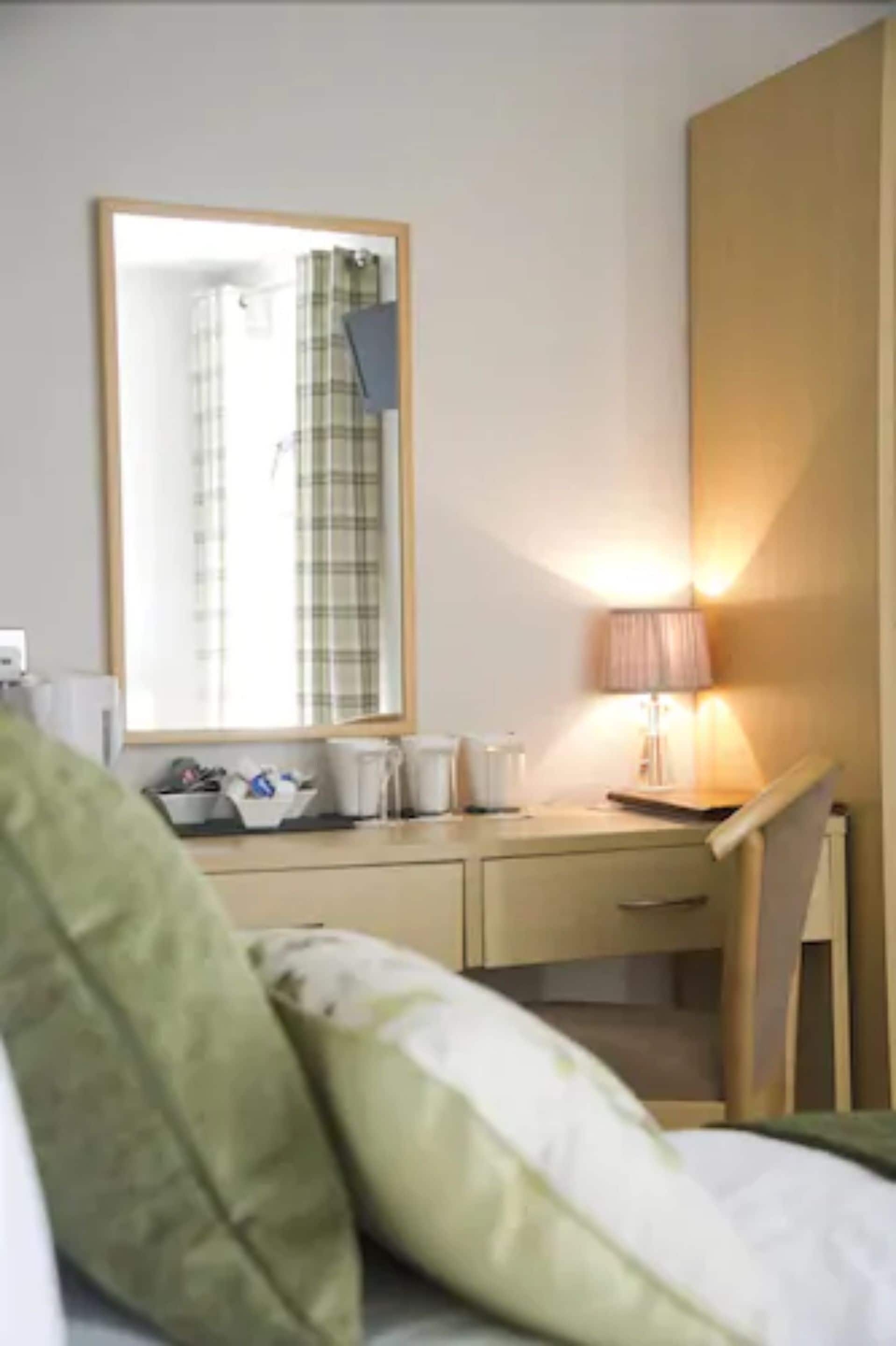 A hotel room with a bed, a desk, a chair, a lamp, and a mirror.
