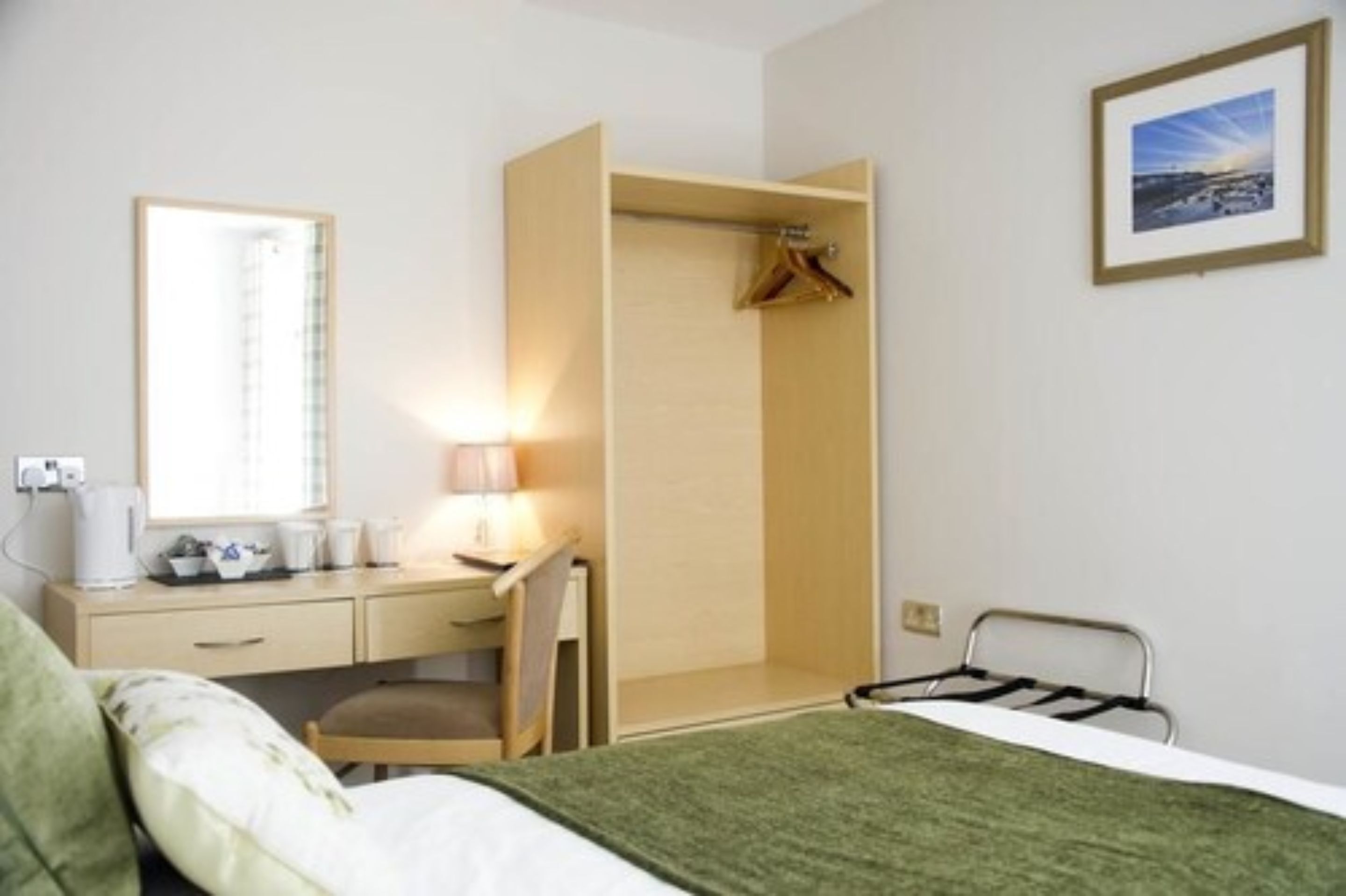 Une chambre d’hôtel comprenant un lit, un bureau avec une chaise, une armoire et une table de chevet avec une lampe.