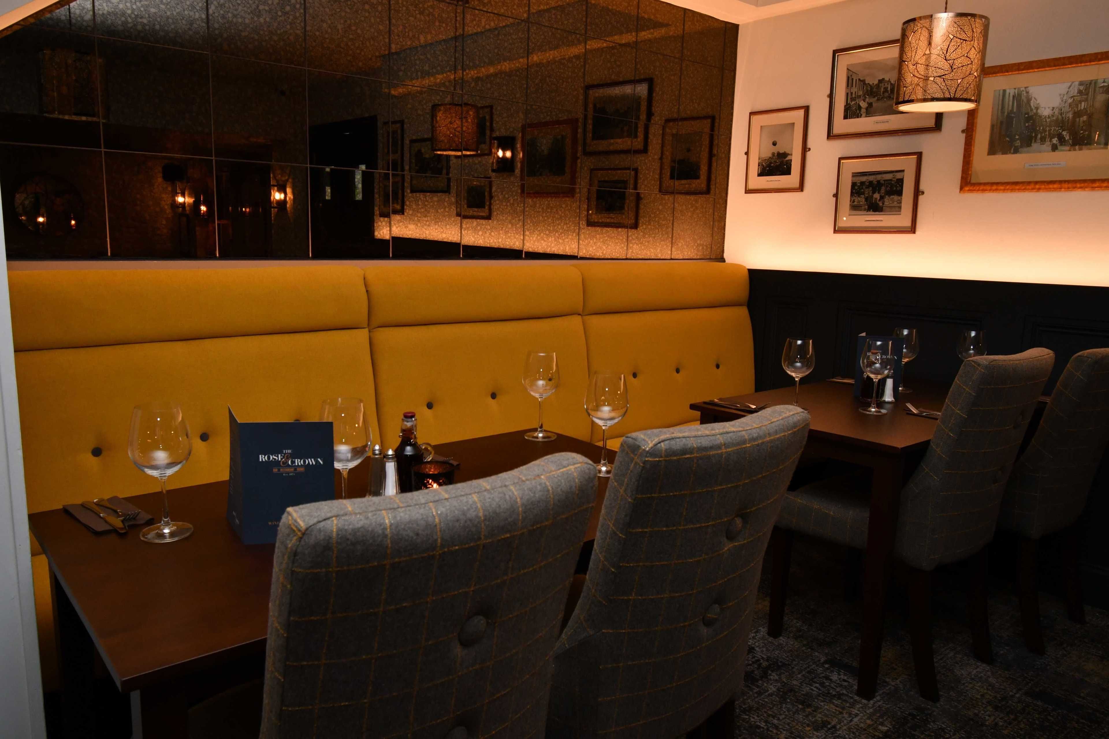 Un restaurante con zona de asientos tipo cabina, una mesa dispuesta con copas de vino y cuadros en la pared.