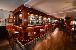 A bar area with wooden bar stools, a counter with bottles, and a television screen.