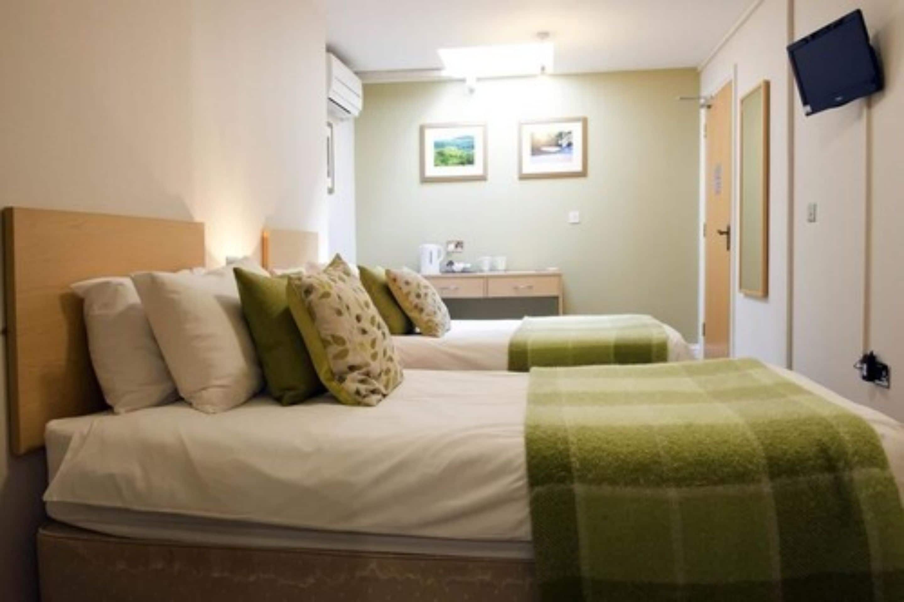 Habitación de hotel con dos camas, un escritorio pequeño y un televisor montado en la pared.