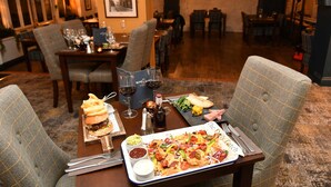 A dining area with a table set for two, featuring a meal tray with nachos, a burger, and a salad. - The Rose and Crown Hotel (Carmarthen)