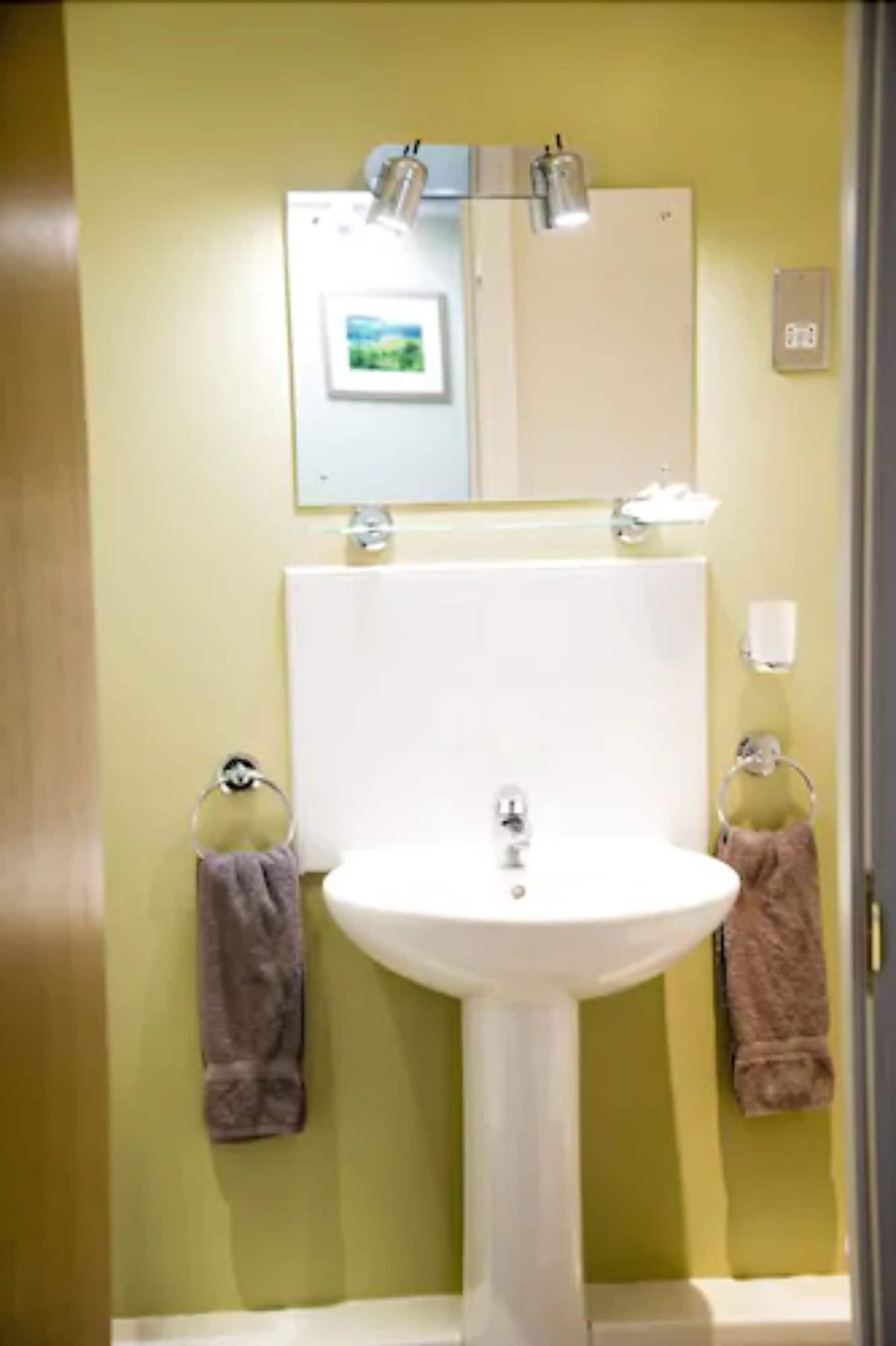 A bathroom with a white sink, a mirror above it, and two towels hanging on towel rings.
