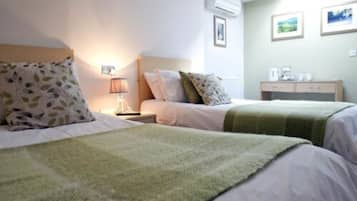 Una habitación de hotel con dos camas, una mesita de noche, una lámpara, aire acondicionado y un armario pequeño.