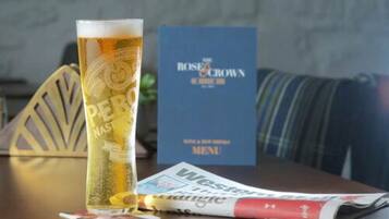 A tall glass of beer with a coaster, a menu, and a newspaper on a table.