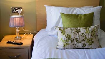 A neatly made bed with white and green pillows, a lamp on a bedside table, and a remote control.