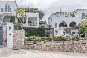 A white building with balconies, stone walls, and potted plants.