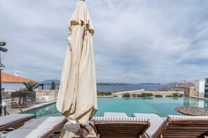A poolside area with lounge chairs and an umbrella, overlooking a body of water and distant mountains.