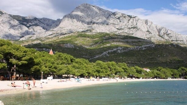 A beach with clear turquoise water, a sandy shore, and a backdrop of rocky mountains. - Apartments Leone (Baska Voda)