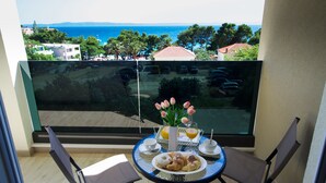 A balcony with a table set for breakfast, overlooking a coastal view with buildings and trees. - Apartments Leone (Baska Voda)