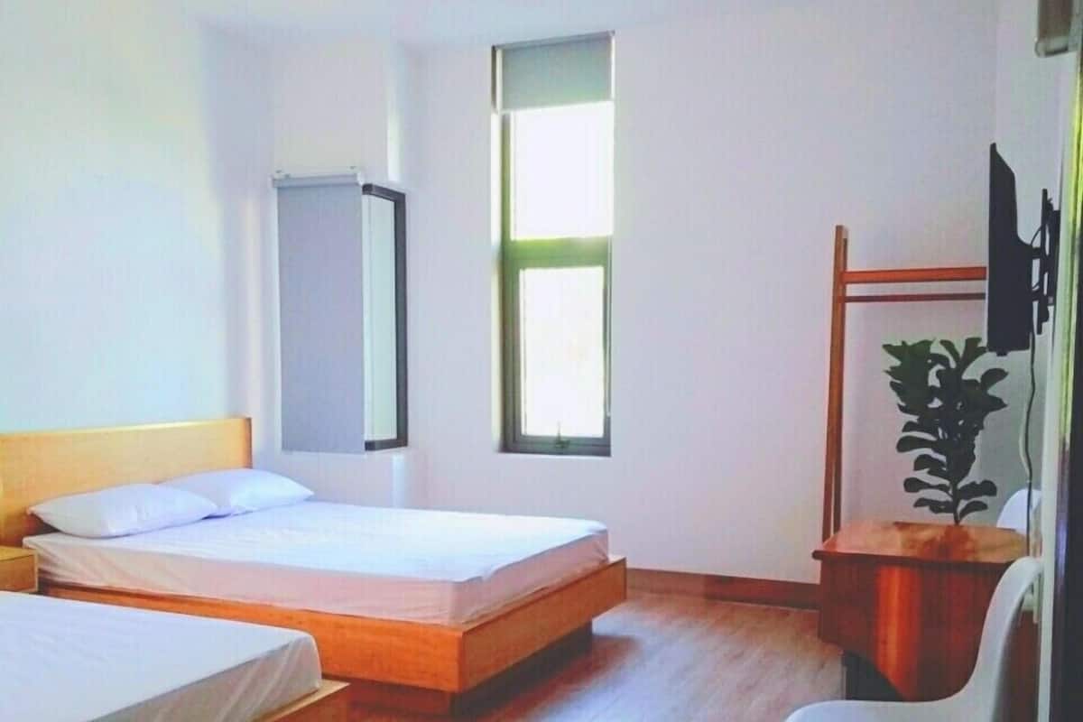 A hotel room with two single beds, a desk, a chair, a TV, and a window.
