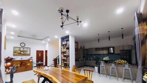 Un comedor amplio con una mesa y sillas de madera, una estantería y una cocina moderna al fondo.