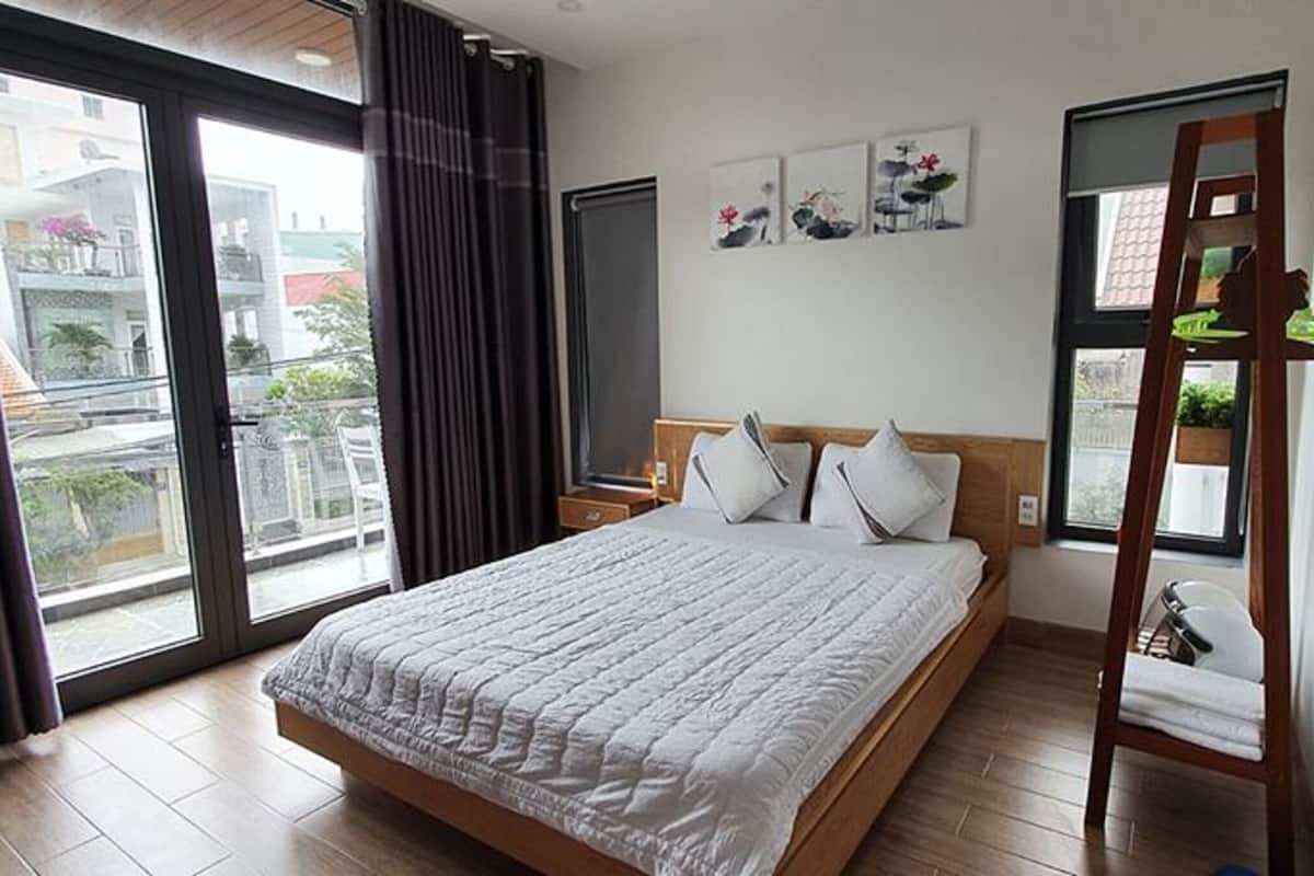 A bedroom with a large bed, a wooden headboard, a nightstand, a window with curtains, and a view of the outside.