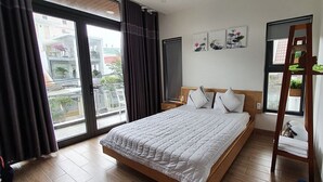 Un dormitorio con una cama grande, cabecera de madera, mesita de noche, ventana con cortinas y vistas al exterior.