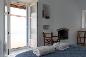 A bedroom with a bed, two chairs, a fireplace, and a view of the beach through an open door.