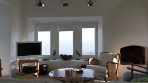 Ein Wohnzimmer mit Fernseher, Kamin und Blick durch große Fenster.