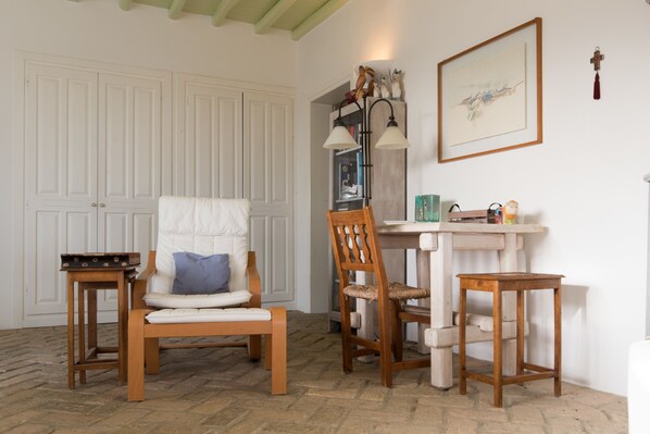 Une pièce comprenant une chaise en bois, une petite table, un meuble contenant des objets décoratifs et un tableau encadré accroché au mur.