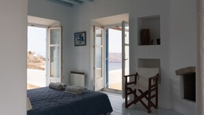 Ein Schlafzimmer mit Bett, Stuhl und Blick auf den Strand durch geöffnete Türen.