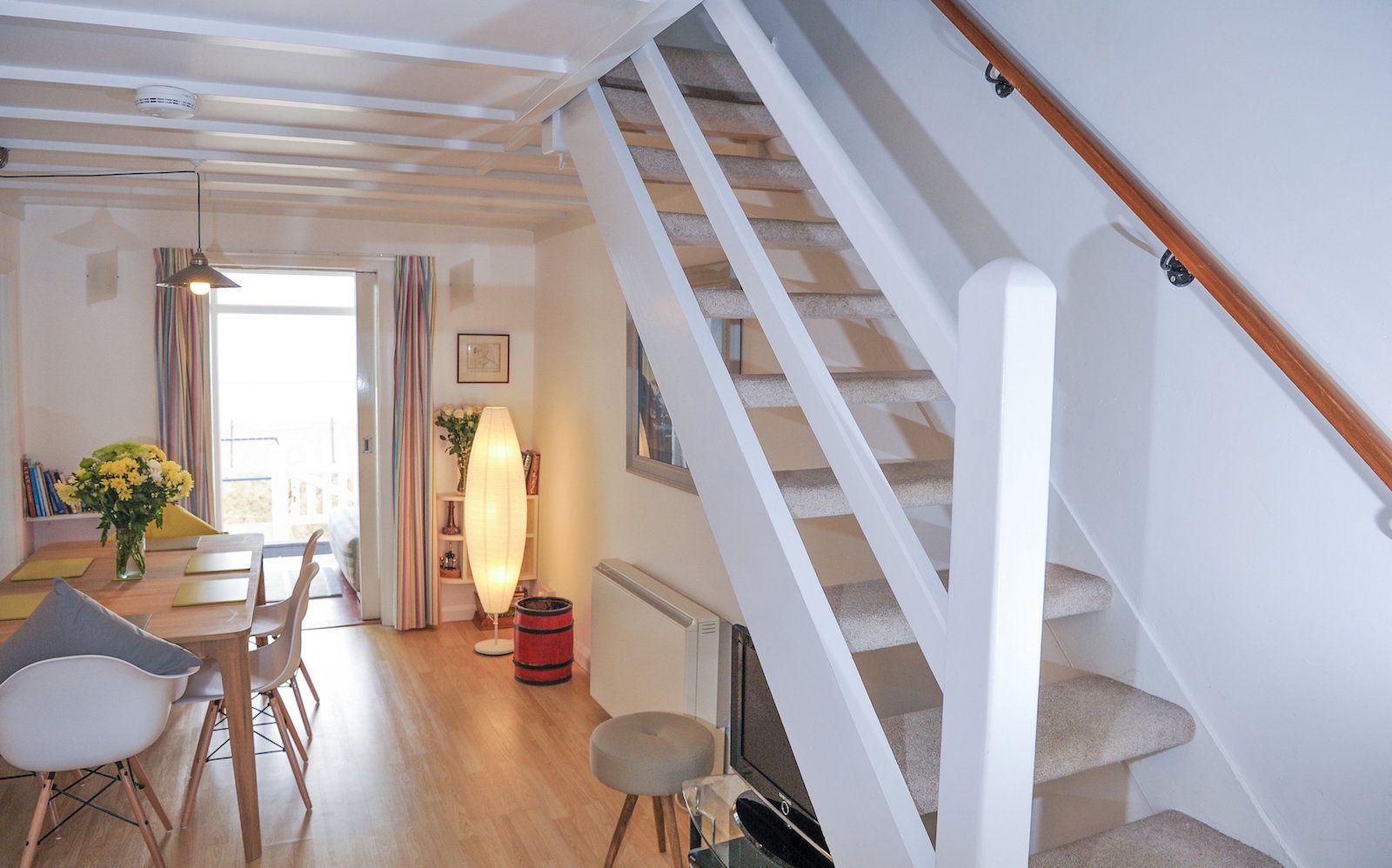 Een moderne woonkamer met een houten trap, een eethoek met een tafel en stoelen, en een groot raam met gordijnen.