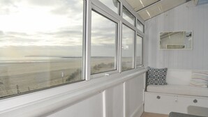 Une pièce dotée d’une grande fenêtre donnant sur une plage, d’un banc blanc agrémenté de coussins et d’un petit miroir accroché au mur.