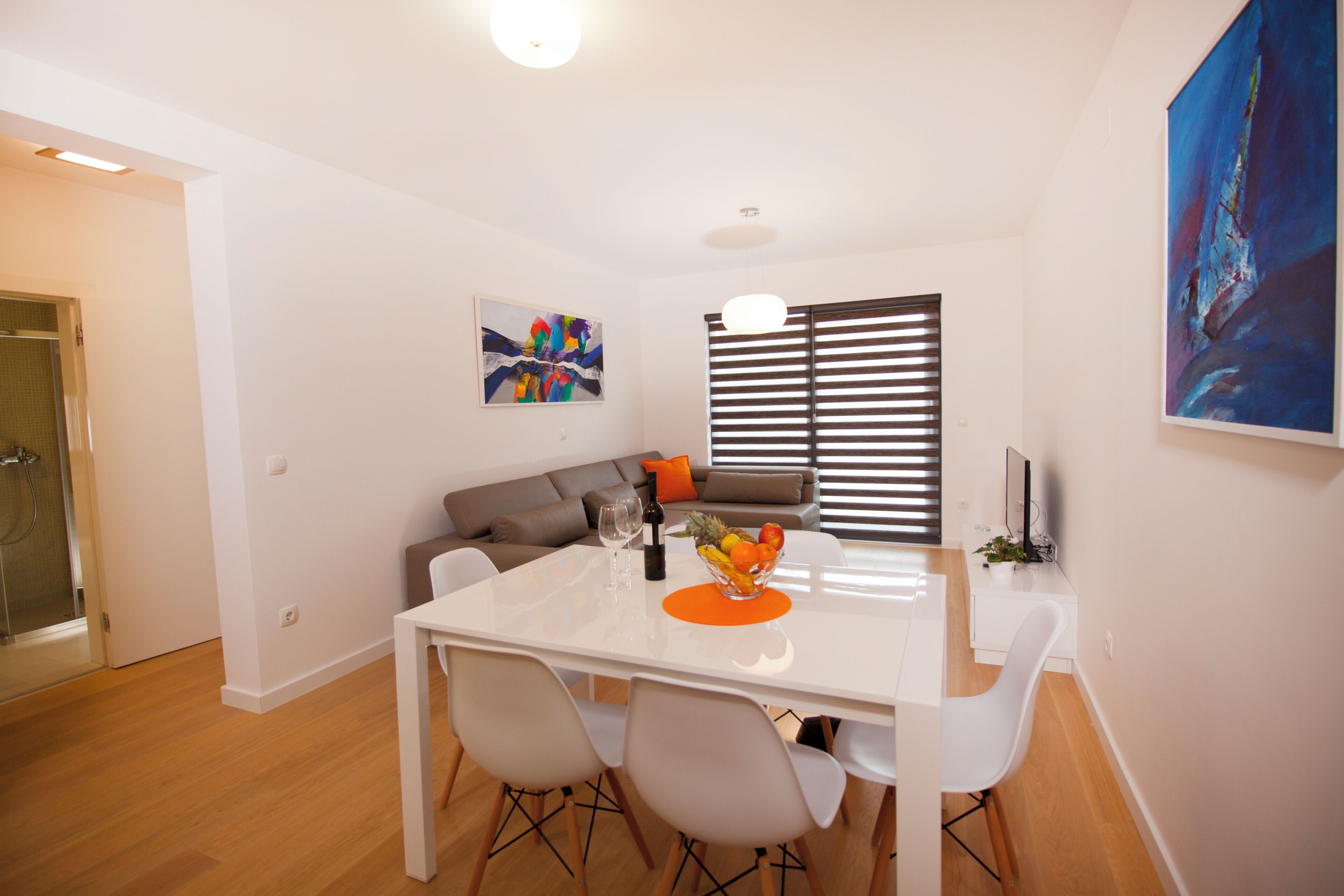 A modern dining area with a white table, four chairs, and a fruit bowl.
