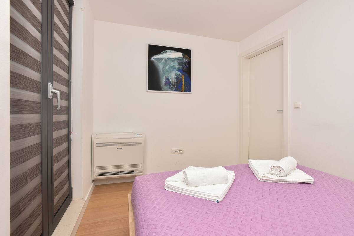 Een slaapkamer met een bed, een wandairconditioner en een deur met een strepenpatroon.