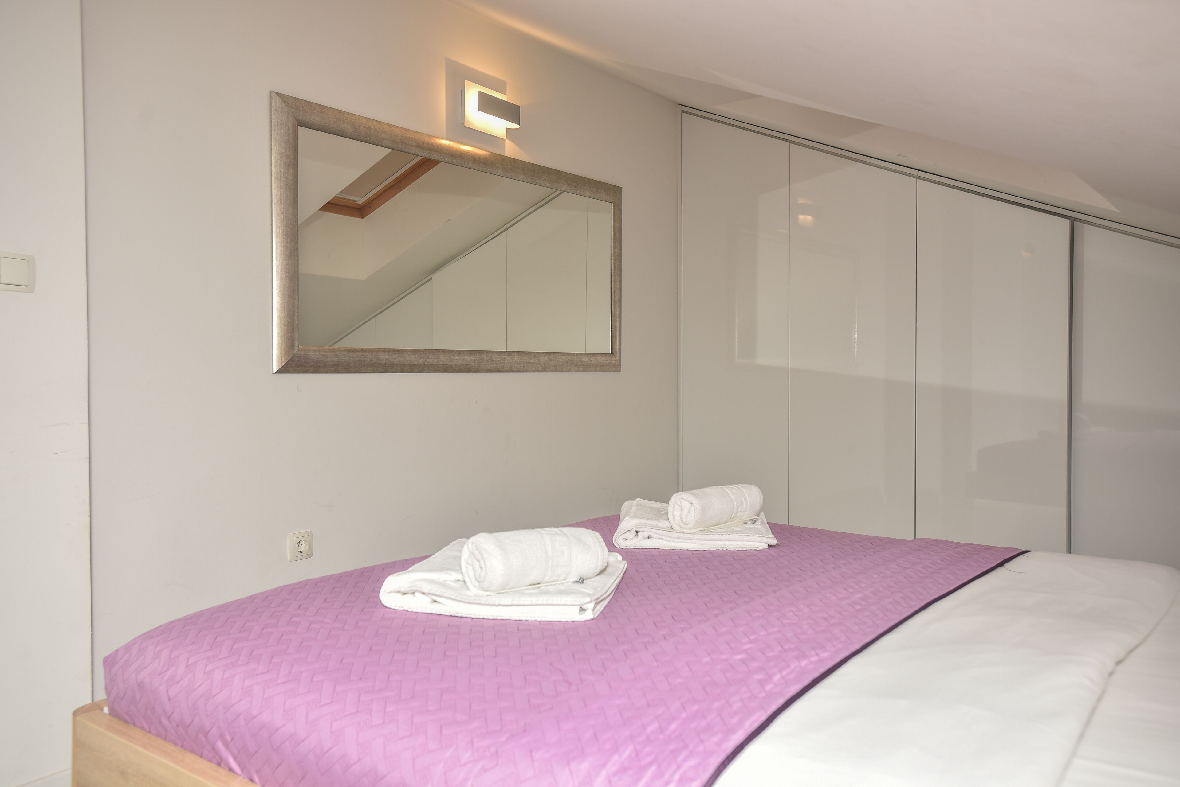 A bedroom with a bed, a large mirror, and a closet.