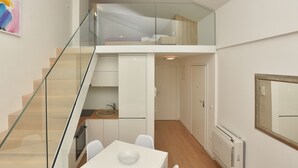 Ein modernes Apartment mit einer Glasstiege, einer Küche mit weißen Schränken, einem Essbereich mit Tisch und Stühlen sowie einer eingebauten Heizung.