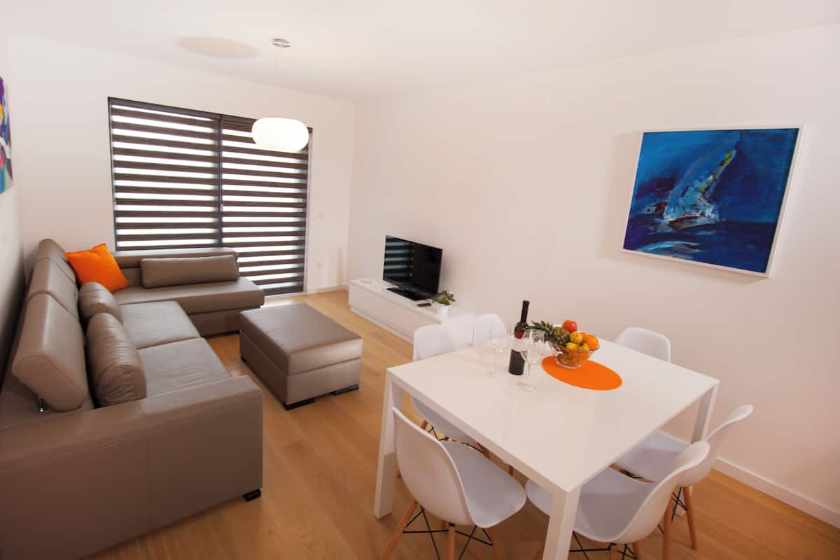 Een moderne woonkamer met een modulaire bank, een eettafel met stoelen, een televisie en kunstwerken aan de wanden.