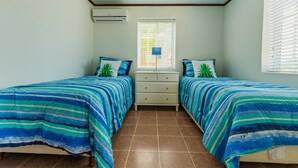 A room with two beds, a white dresser, a ceiling fan, and a window with blinds. - Old Aloe House (Savaneta)