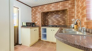 A compact kitchen with a brick backsplash, a microwave, a toaster, and a sink. - Old Aloe House (Savaneta)