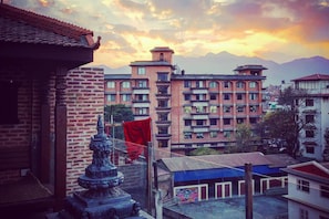 A view of a residential area with multi-story buildings, a traditional building with a tiled roof, and a statue in the foreground. - Tara Art House (Lalitpur)