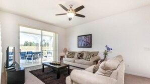 A living room with a beige sofa, a coffee table, a TV stand, and a ceiling fan.