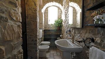 A bathroom with stone walls, a white sink, two toilets, and a window with a plant.