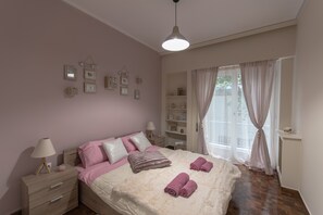 A bedroom with a bed, bedside tables, a lamp, a shelf with decorative items, and a window with curtains.