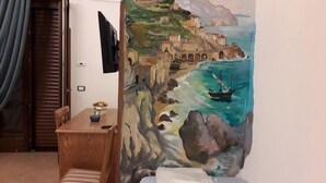 Una habitació amb taula de fusta, una cadira, un quadre d'una escena costanera i un televisor fixat a la paret.