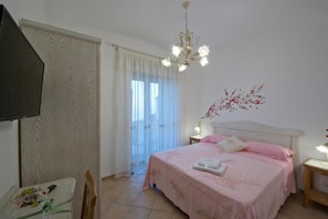 A bedroom with a bed, a nightstand, a chair, a table with a vase, and a window with curtains. - B&B Il Casale Del Generale (Agerola)