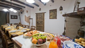 Una zona de menjador amb una taula llarga preparada per a una posta, que inclou una varietat de fruites, pastissos i una gerra de suc.