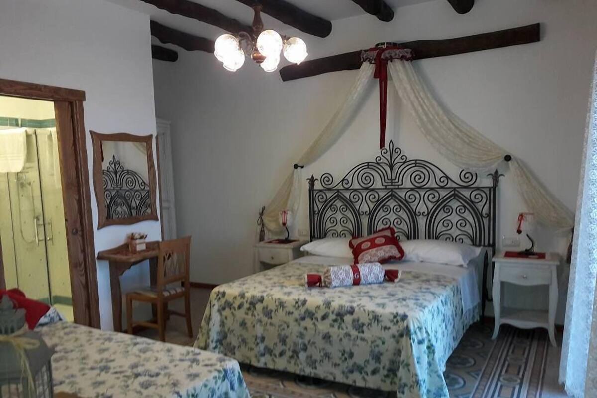 Ein Schlafzimmer mit einem Himmelbett, einem Nachttisch, einem Sessel und einem kleinen Tisch mit einer Lampe.