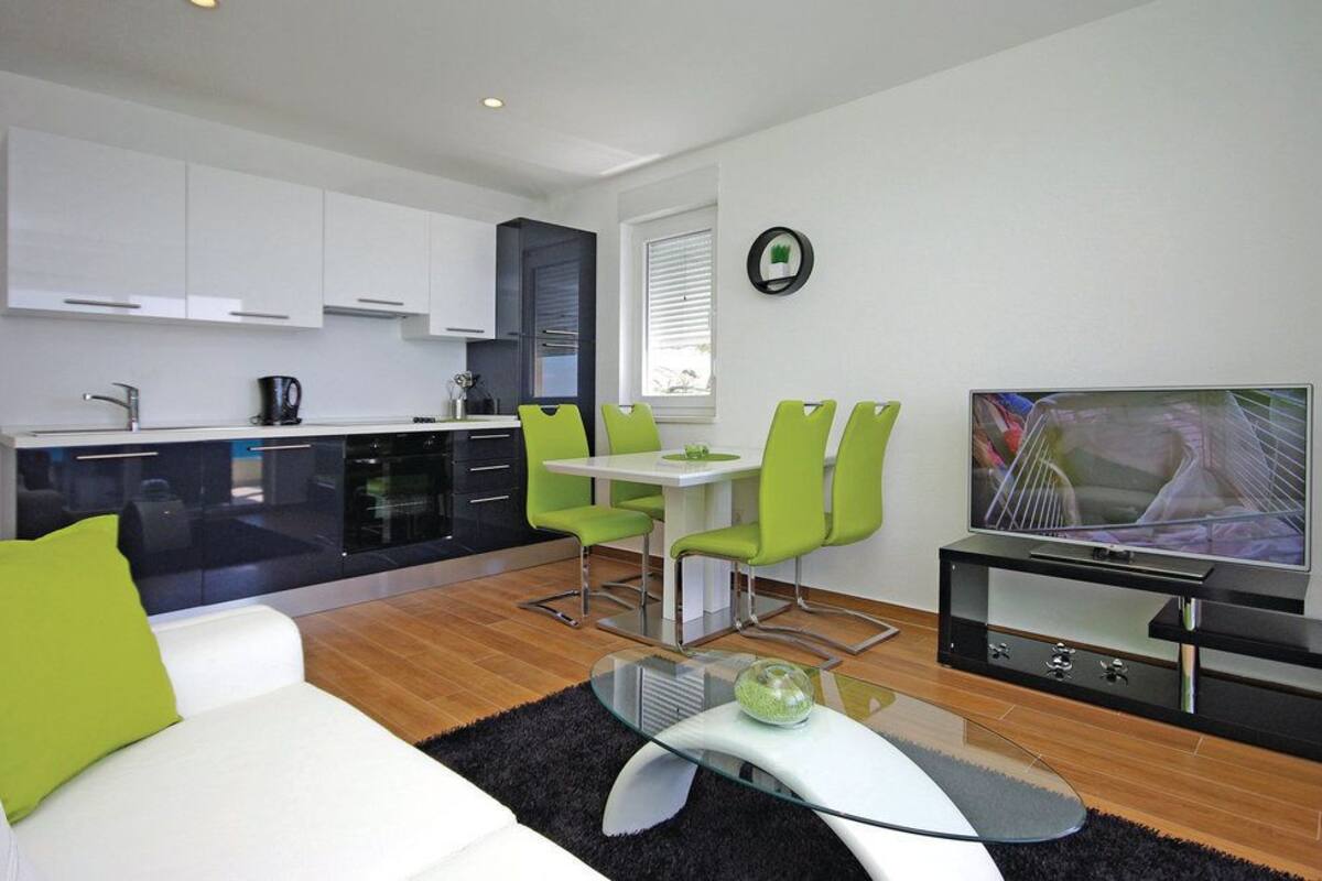 Une cuisine moderne avec des meubles blancs, un coin repas avec des chaises vertes, un téléviseur à écran plat et une table basse en verre.