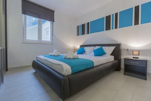 A modern bedroom with a large bed, a nightstand, and a window with blinds. - Lux Apartments (Makarska)