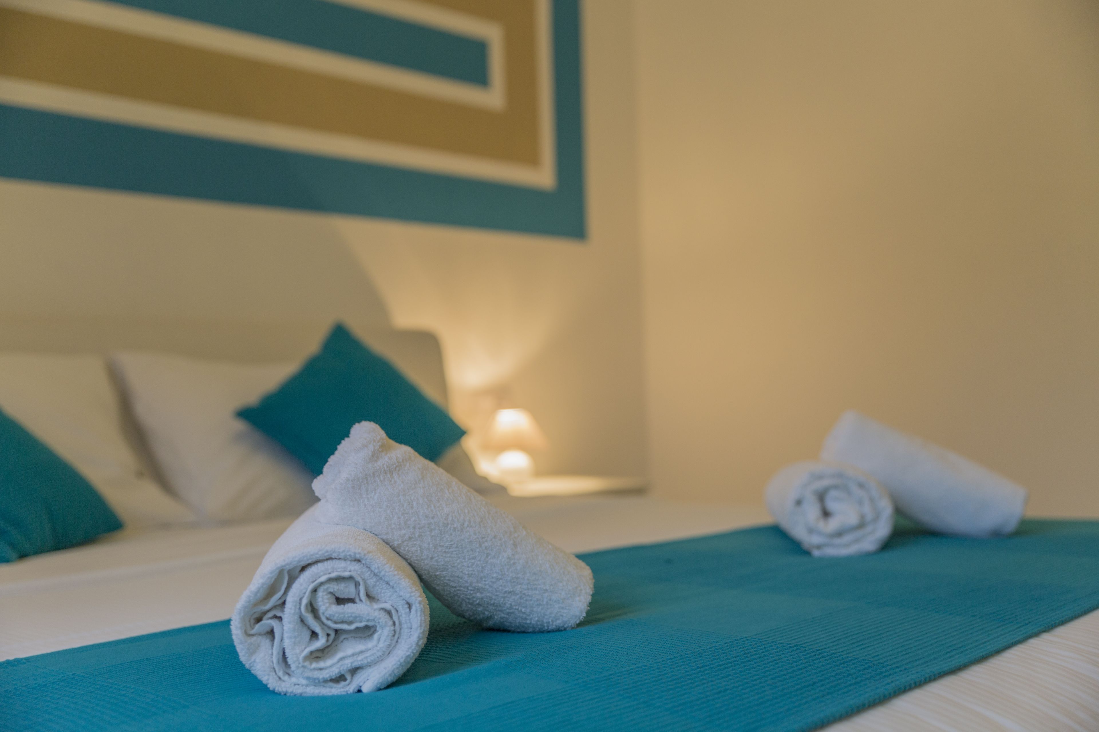 A neatly made bed with a teal bedspread and white towels rolled up at the foot.