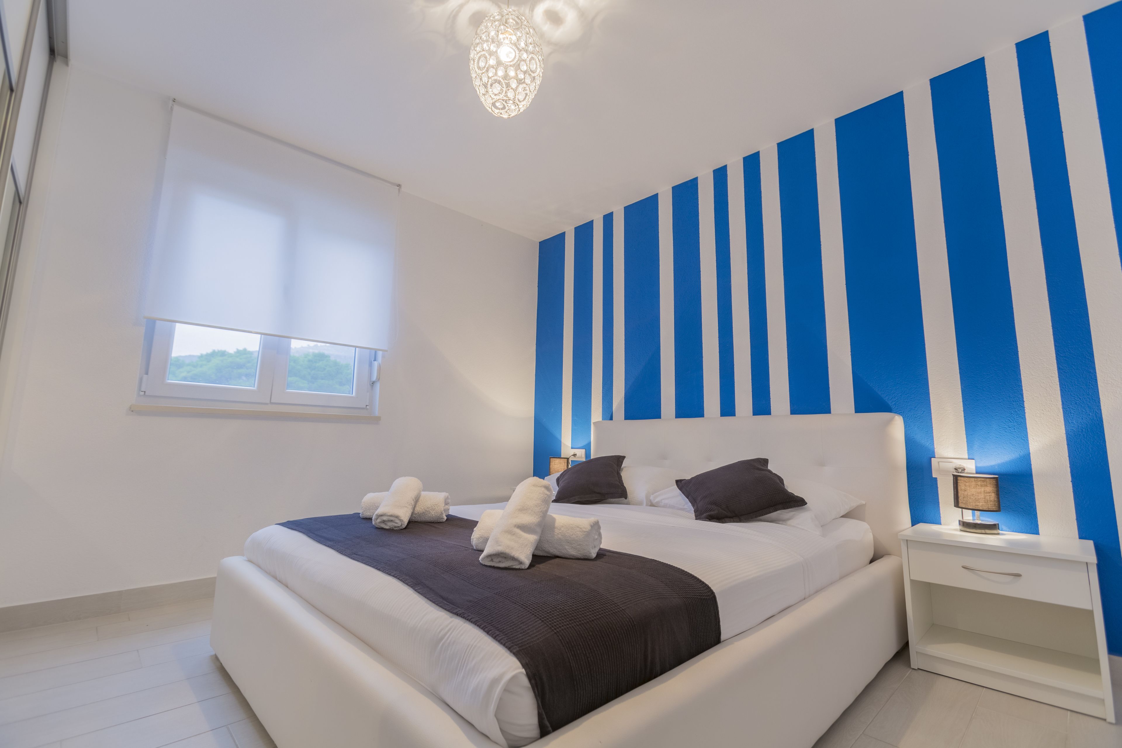 A modern bedroom with a large bed, a nightstand, a lamp, and a window with blinds.