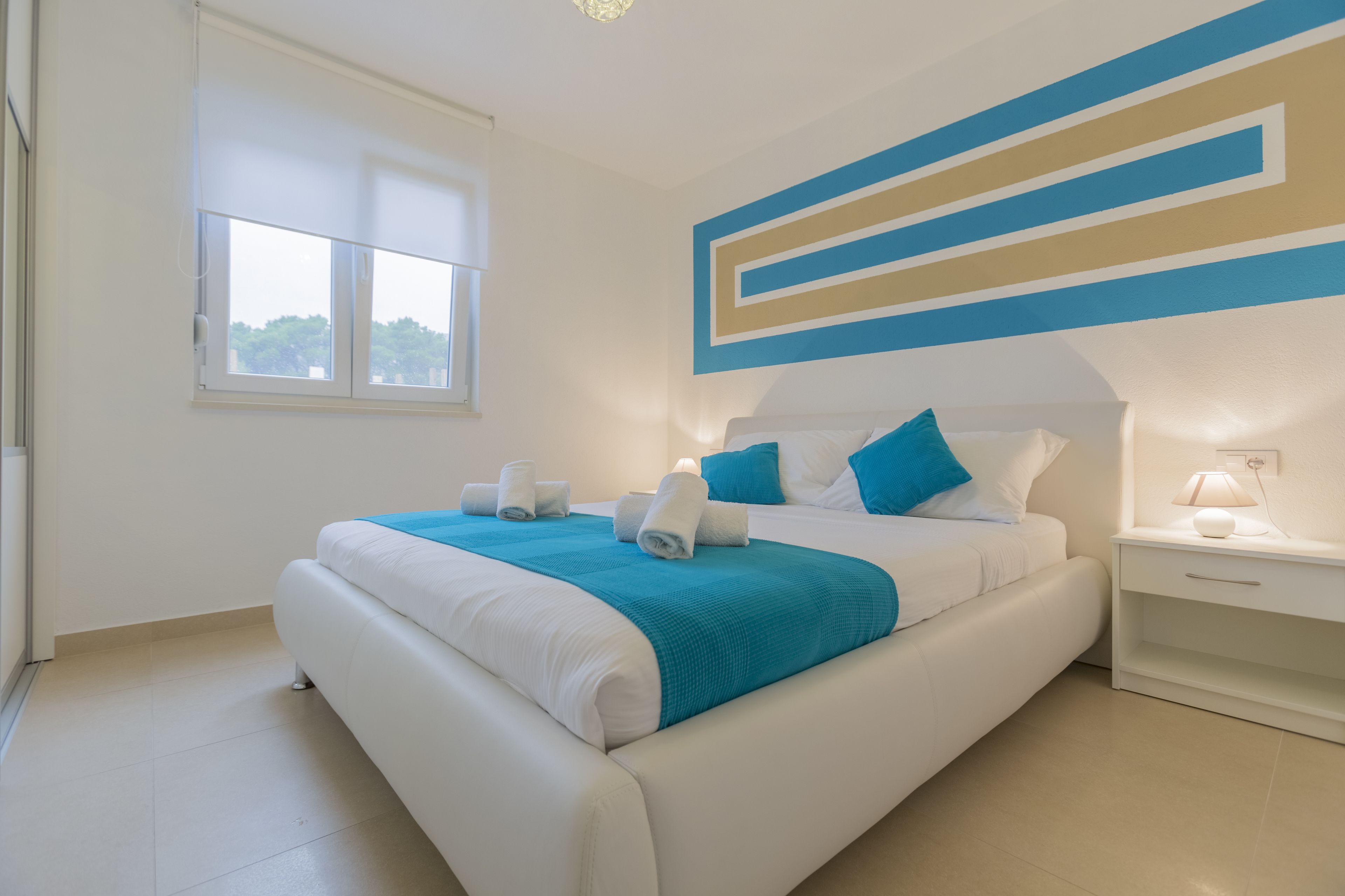 Un dormitorio moderno con una cama grande, una mesita de noche, una ventana y una pared con diseño geométrico.